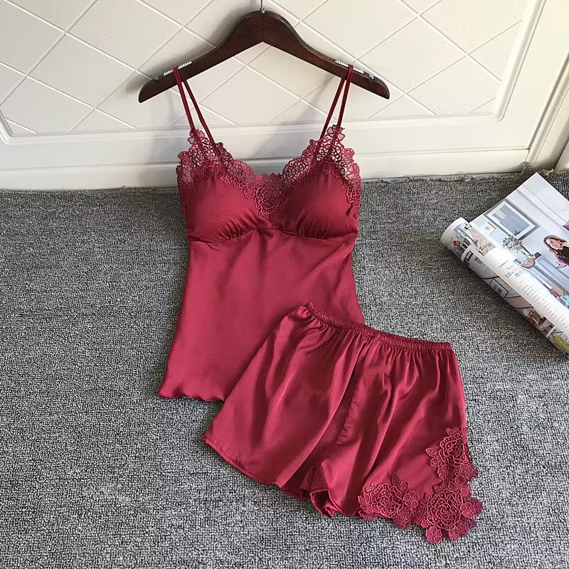 Women’s wine‑red satin camisole‑shorts pajama set, double thin spaghetti straps, V‑neck decorated with rose‑pattern hollow lace, built‑in chest padding, elastic‑waist shorts with large floral lace appliqués on side hem, smooth glossy fabric, elegant romantic night loungewear.