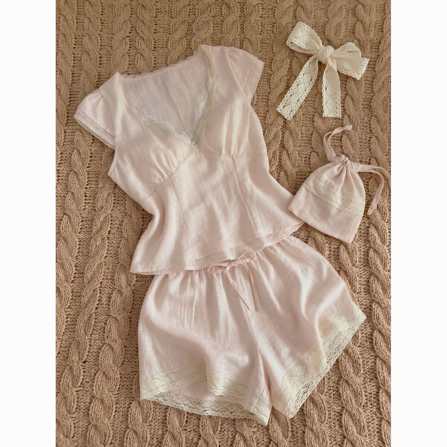 Women’s light‑pink short‑sleeve & shorts pajama set, textured breathable fabric, V‑neck trimmed with delicate lace, fitted waist top, drawstring shorts with lace hem, comes with matching lace bow and small storage pouch, vintage cottage‑style loungewear.